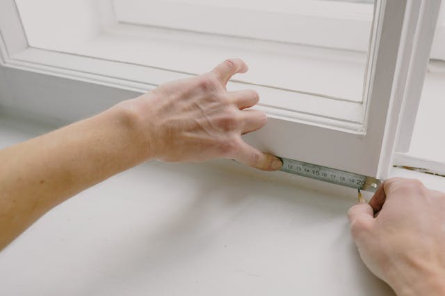hands measuring a windowsill with a tape measure